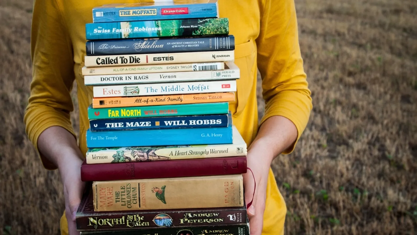 A stack of business books on an office desk next to a notebook and a cup of coffee.