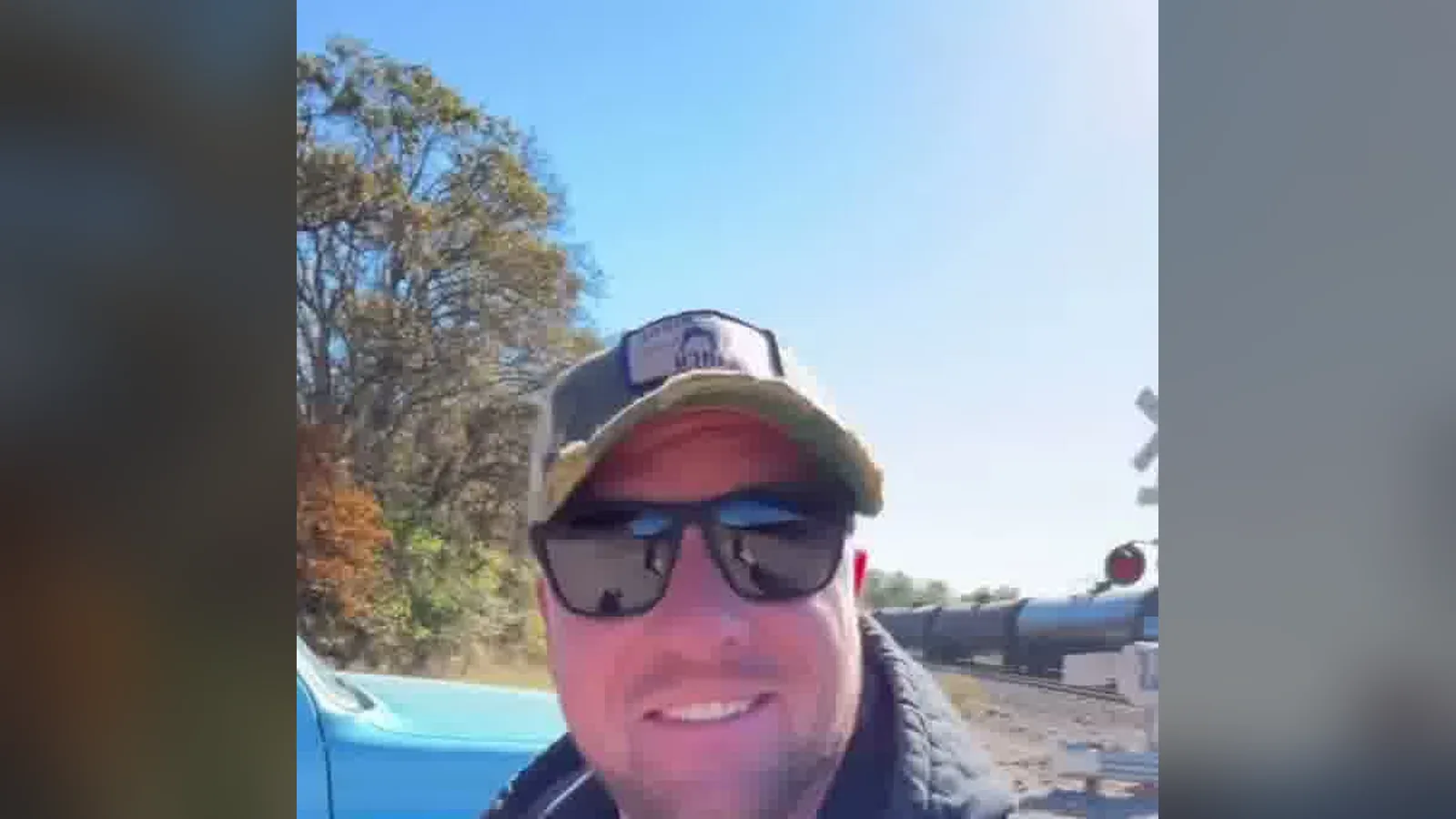 Ryan Stewman of @hardcorecloser smiling by a railroad crossing as a freight train passes, from one of his Instagram reels.